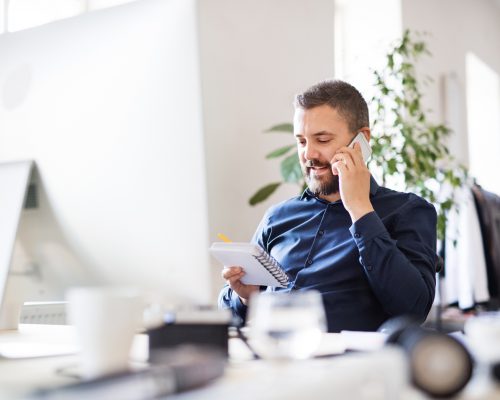 Businessman In Wheelchair At The Desk In His Office.