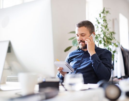 Businessman In Wheelchair At The Desk In His Office.